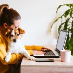 a woman working on a laptop while holding her puppy in her lap